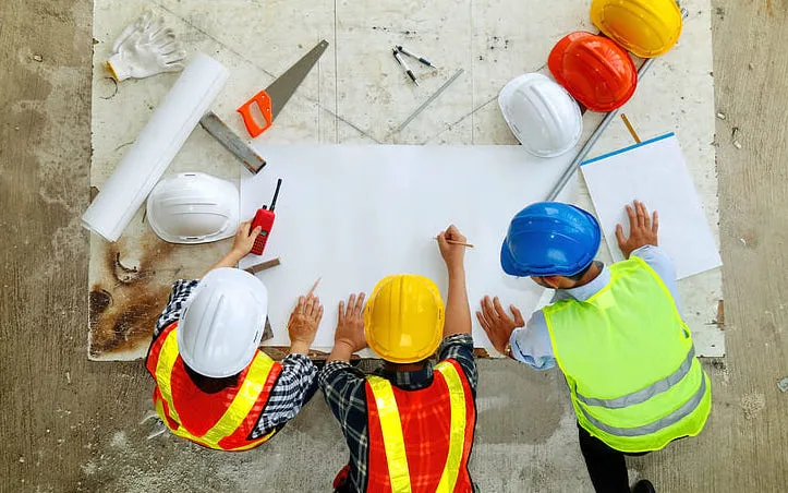 Team of engineers in hard hats working on plans, seen from above